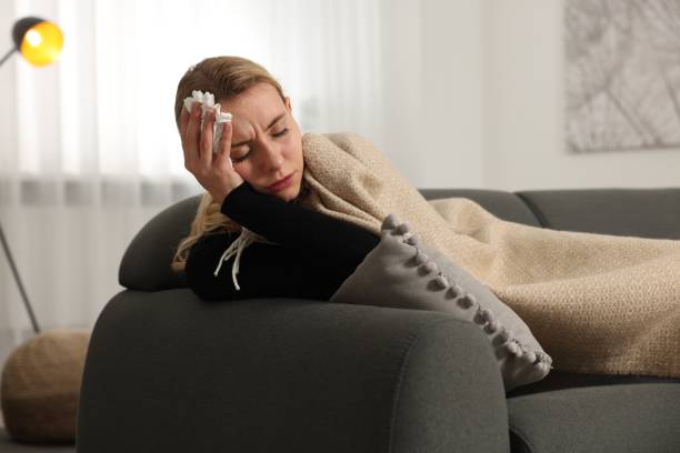 istock Sick woman with tissue under blanket on sofa at home. Cold symptoms 1855708232