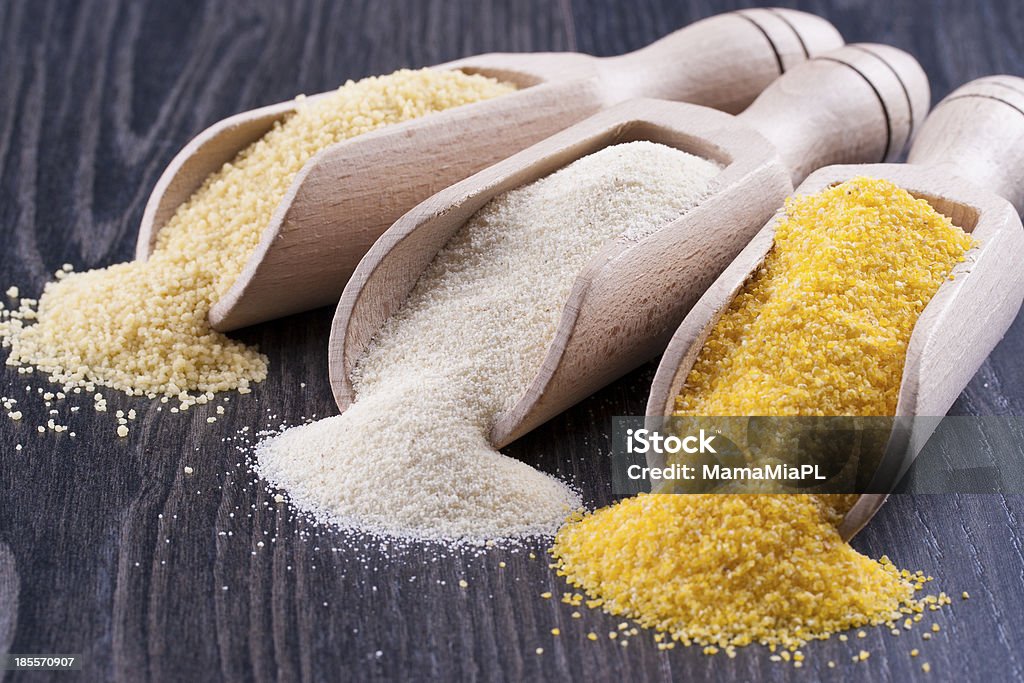 Groats Close up photo of a raw eco food in the wooden spatulas - light yellow couscous, light brown farina and dark yellow cornmeal placed on a dark wooden background. Backgrounds Stock Photo