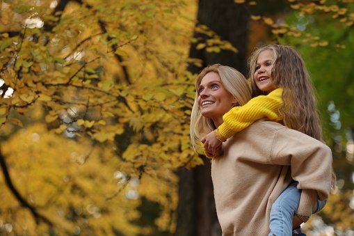Portrait of happy mother and daughter in autumn park. Space for text