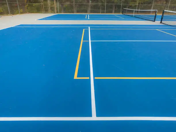 Photo of Close up photo of a outdoor blue tennis court with white lines combined with yellow, gold, pickleball lines.