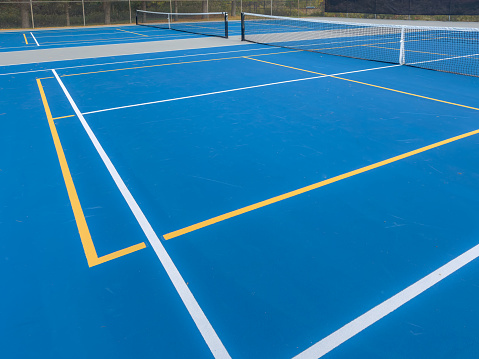Close up photo of a outdoor blue tennis court with white lines combined with yellow, gold, pickleball lines.