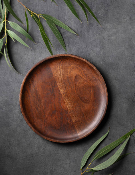 istock Wooden empty plate with green leaves on a dark gray background. 1855724728