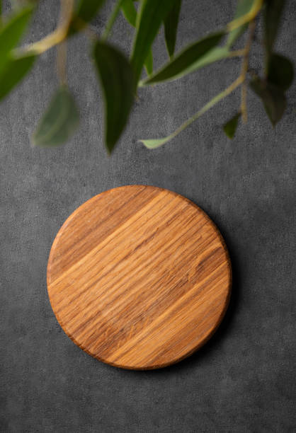 istock Wooden empty round board with green leaves on a dark gray background. 1855724732