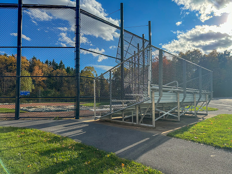 Photo of typical angle frame bleacher and backstop at a nondescript high school softball field. No people visible. Not a ticketed event.