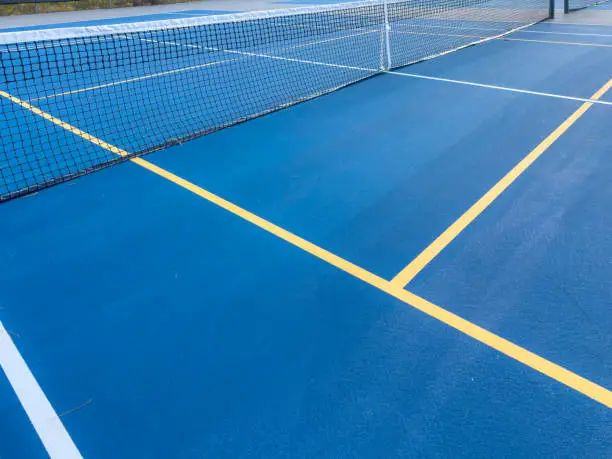 Photo of Close up photo of a outdoor blue tennis court with white lines combined with yellow, gold, pickleball lines.