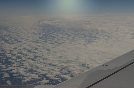 wing of an airplane with clouds below and sun in the background, flying above the clouds