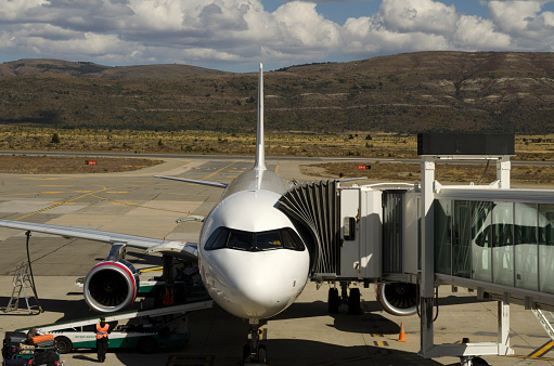 Airplane at the airport with the sleeve waiting for passengers and cargo, recharging with fuel, with mountains in the background