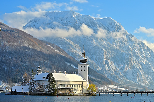 The romantic world famous Ort lake castle on an island on Lake Traunsee in Gmunden in winter with snow and the mountain Traunstein in the background