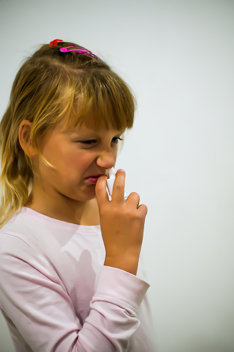 little embittered  girl in pajamas sprays her nose with anti-pneumonia spray - blurred background.