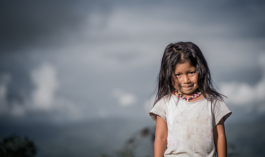 portrait of an indigenous girl with a very serious face while outdoors in a cloudy sky