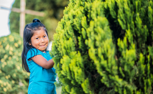 Portrait of little girl playing and smiling looking at the camera while outdoors playing with a tree.