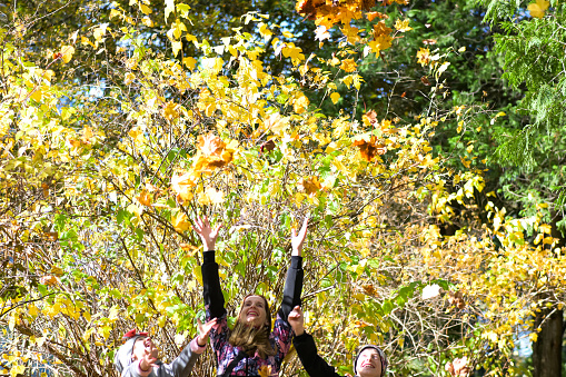 a young smiling family with small children throwing autumn leaves into the air.