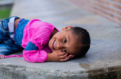 portrait of a little girl playing lying on the ground in the open air while smiling and holding her hands next to her face