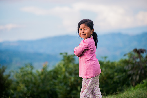 small indigenous girl standing outdoors in a beautiful landscape with her hands folded