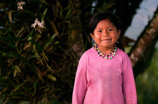 small indigenous girl in the open air with a tree in the background while wearing a necklace and smiling