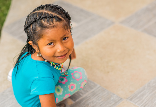 portrait of little indigenous girl playing outdoors sitting on the floor while looking at the camera