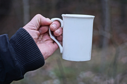 hand of a man in black clothes holding a white ceramic cup with coffee on the street