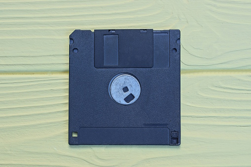 one old black square plastic computer floppy disk lies on a yellow wooden table