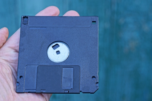 one old black square plastic computer floppy disk lies on the palm of the hand on a green background