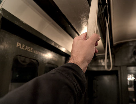 hand holding a strap on a subway car close up (vintage old time historic antique rail) man, straphanger, commute, commuter riding train (history, past, black and white) metro handle