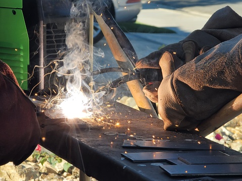 A stock photograph of a welder at work welding. In this picture, you can see hands working on a metalwork project. The picture is taken up close with limited background.
