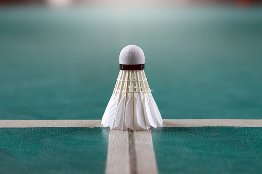 Cream white badminton shuttlecock and racket on floor in indoor badminton court, copy space, soft and selective focus on shuttlecocks.