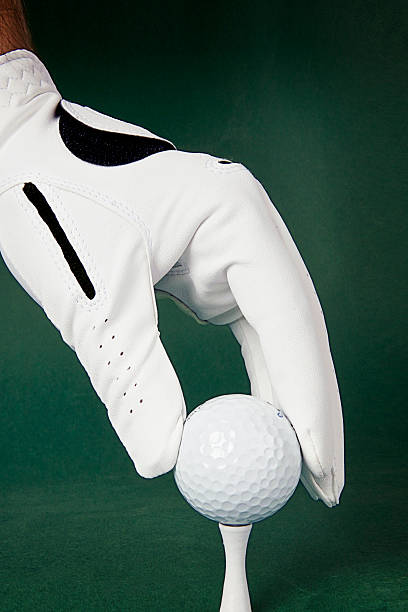 istock Golfer's hand in white gloves with a ball on green. 185599359