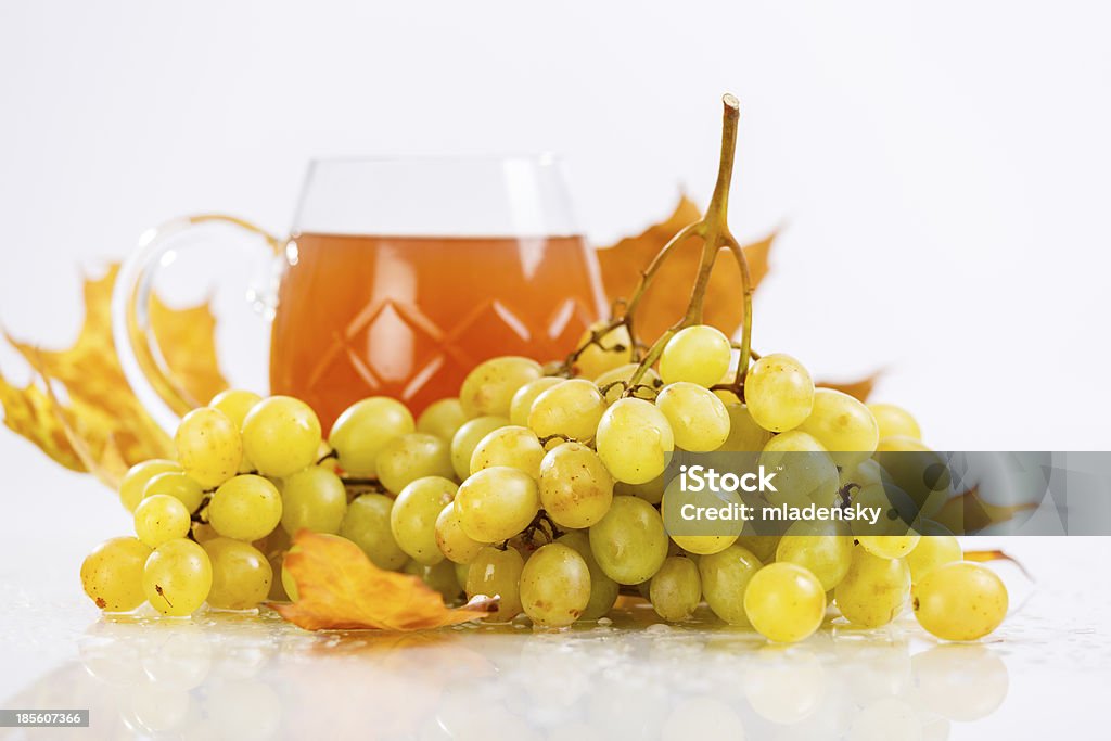 Glass of wine with grapes and leaves Filled glass of white wine with grapes and leaves on white background. Agriculture Stock Photo