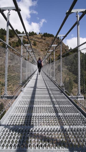young curvy caucasian girl crossing the canillo suspension bridge in andorra on a sunny day hiking in the mountains