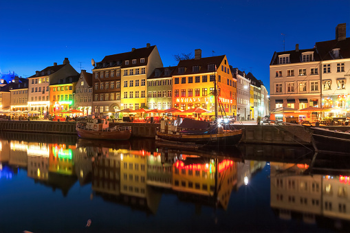 Nyhavn Canal and colorful businesses in central Copenhagen, Denmark at night. Nyhavn is a 17th-century waterfront and entertainment district lined by brightly colored bars, cafes and restaurants.