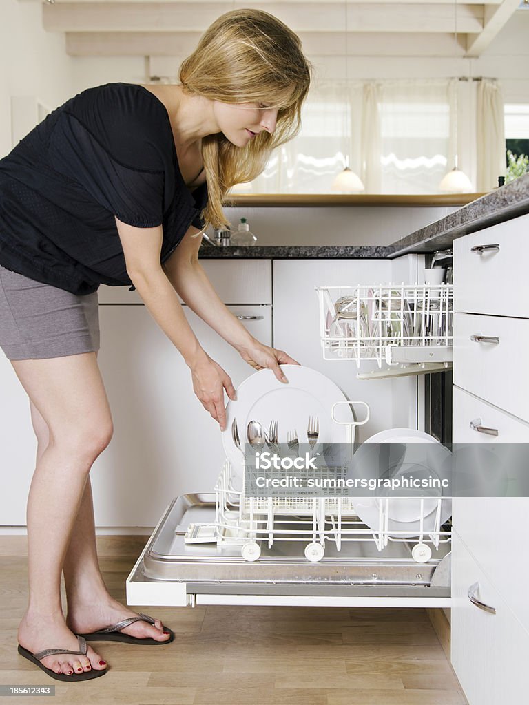 Female emptying the dishwasher Photo of a blond female leaning over and unloading her dishwasher. Dishwasher Stock Photo