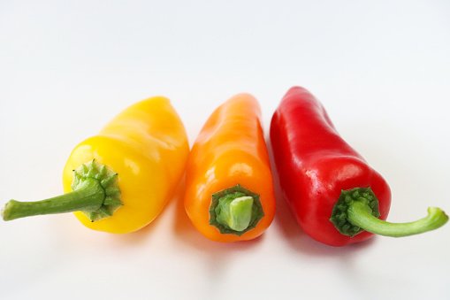 Stock photo showing close-up view of row of three, alternating yellow, orange and red mini peppers (Capsicum annuum) on white background, modern minimalist poster wallpaper background design.