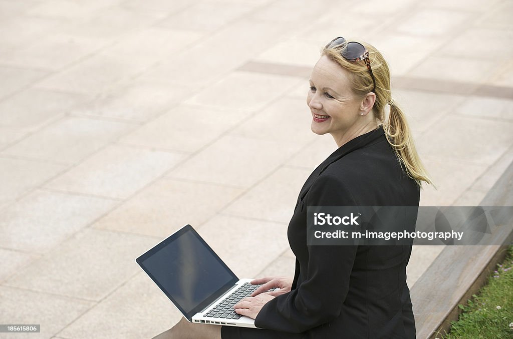 Donna d'affari sorridente con il portatile, all'aperto - Foto stock royalty-free di Abbigliamento elegante