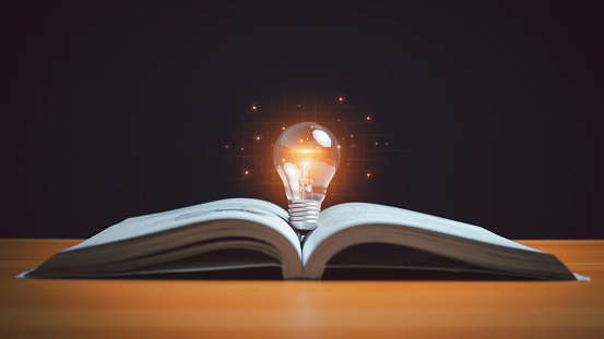 Glowing light bulb in mid-air over the blank books on a shelf against blue wall with copy space.