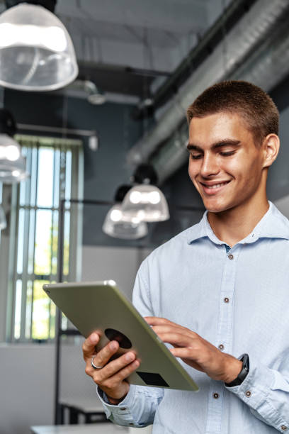 istock Young handsome businessman using digital tablet while standing in the office 1856173406