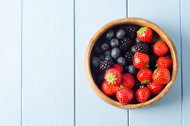 Summer Fruit Bowl Overhead A shabby old wooden bowl of Summer berry fruits shot from above, on a freshly painted pale blue wood planked table. fruit bowl stock pictures, royalty-free photos & images