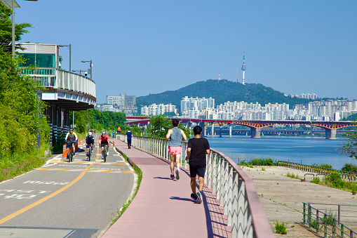 Seoul, South Korea - June 2, 2023: Along the stretch of Jamwon, nestled between Olympic Boulevard and the river, joggers and cyclists enjoy the paths with Seongsu Bridge, Namsan Mountain and Tower.