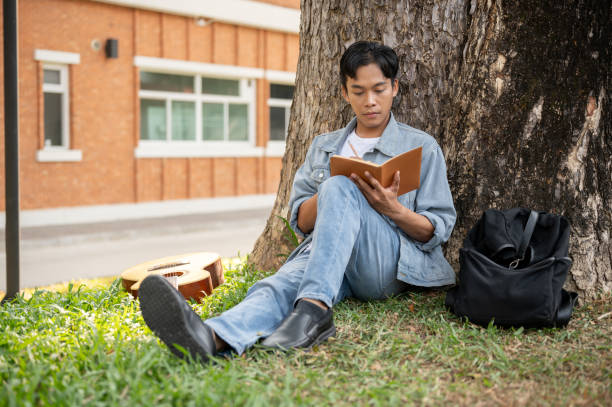 istock A focused Asian male student is reading a book or writing some ideas in a book under the tree. 1856283209