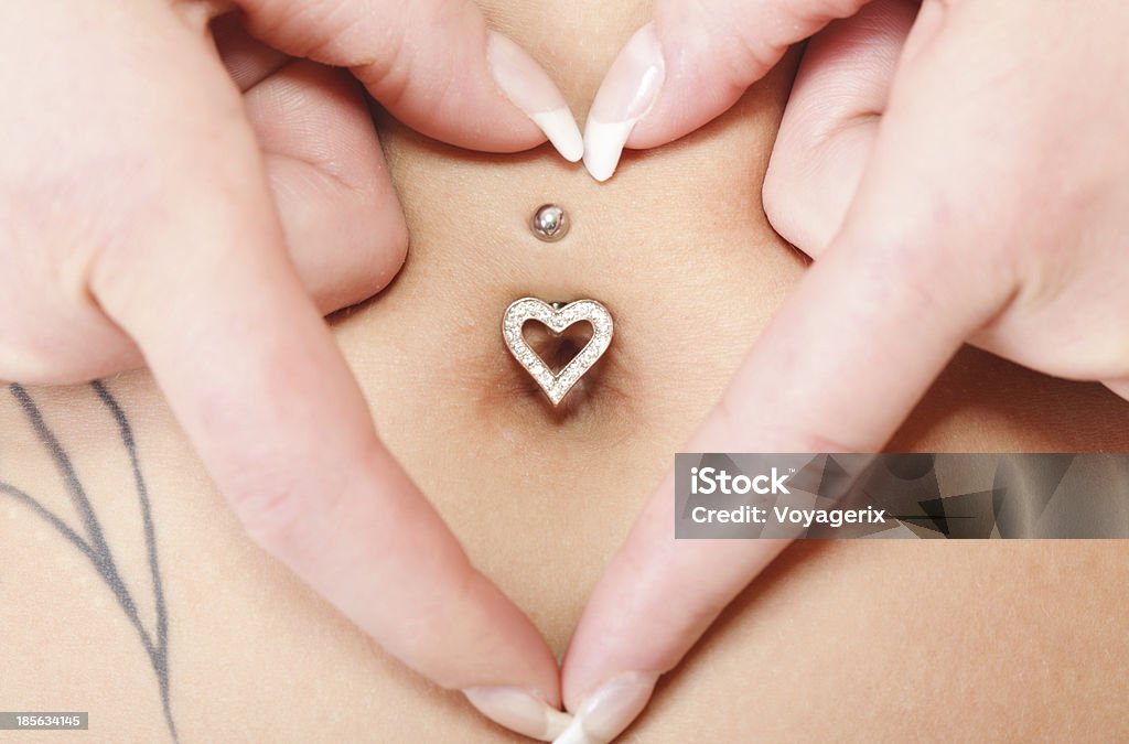 hands heart symbol around navel piercing woman's hands forming a heart symbol around navel with piercing. Mother awaiting for the baby. Abdomen Stock Photo