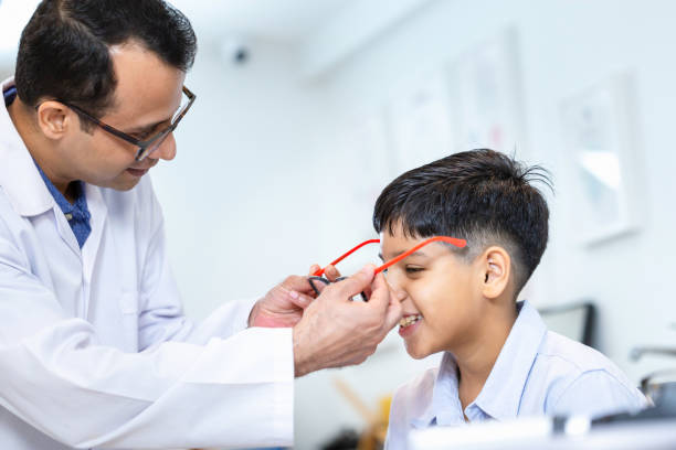 istock Boy doing an eye test checking examination with optometrist in the optical shop, Smiling Indian-thai boy choosing glasses in an optics store 1856357573