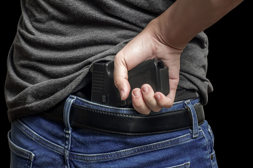 Man drawing a conceal carry pistol from a holster isolated on black background