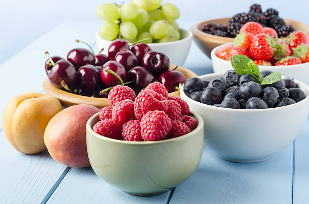 Fruit Harvest Selection in Bowls A selection of different Summer fruits, in a variety of bowls on a painted blue wood planked farmhouse kitchen table, against a light blue background. fruit bowl stock pictures, royalty-free photos & images