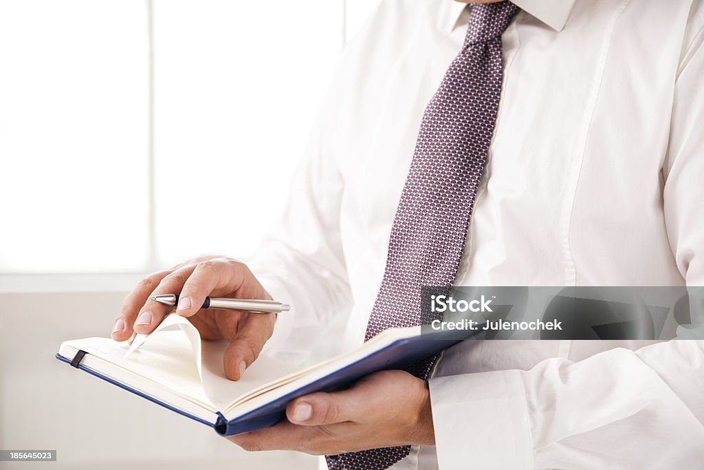 Businessman standing in office holding diary Businessman standing in office holding diary on white Adult Stock Photo