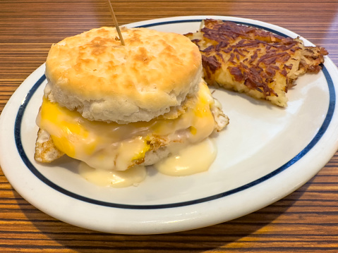 Egg and cheese inside of a biscuit sandwich with hash brown on a wooden table