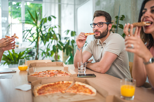 Diverse employees enjoying a relaxed lunch break with pizza and refreshing drinks in a contemporary office setting.
