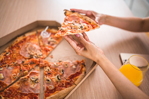 Colleagues of diverse backgrounds share a freshly delivered pizza, engaging in a moment of relaxed camaraderie at work.