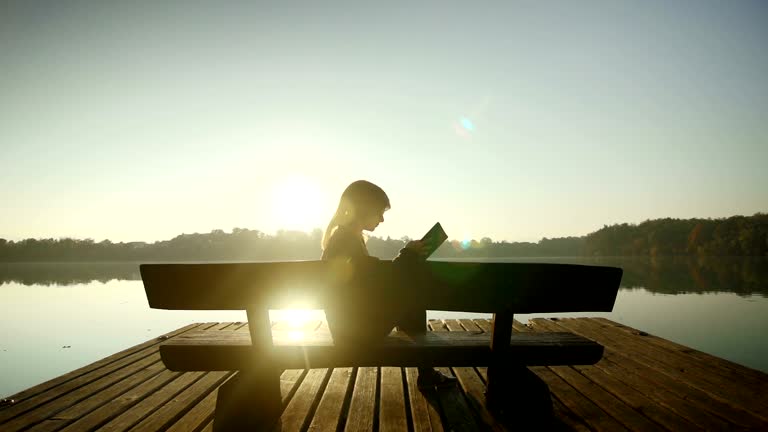 Young woman reading a book by the lake