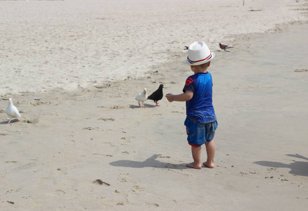 View from above - sea waves and happy relaxed boy lay on the sand with stretched hands wearing sunglasses