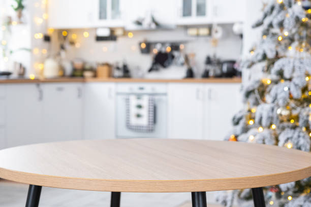istock Round empty table to demonstrate the product with space for text in white kitchen, modern interior with a Christmas tree and fairy lights. New Year, Christmas mood, cozy home. 1856592420