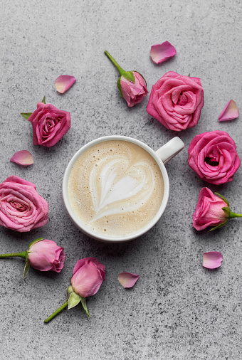Round frame of  pink roses and cup of coffee on concrete background.